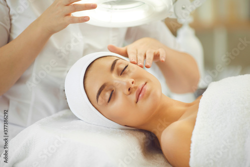 Smiling young womans face under light getting and enjoying facial massage from cosmetologist