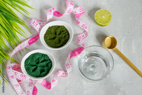 Chlorella and spirulina powder on a light background. A green superfood detox for a vegetarian diet. Healthy lifestyle concept. Measuring tape for the figure