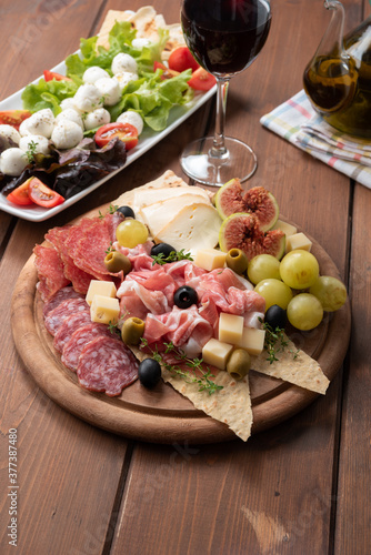 Tipico tagliere di antipasti misti con prosciutto crudo, salame, formaggi, olive e frutta fresca, Cucina Italiana