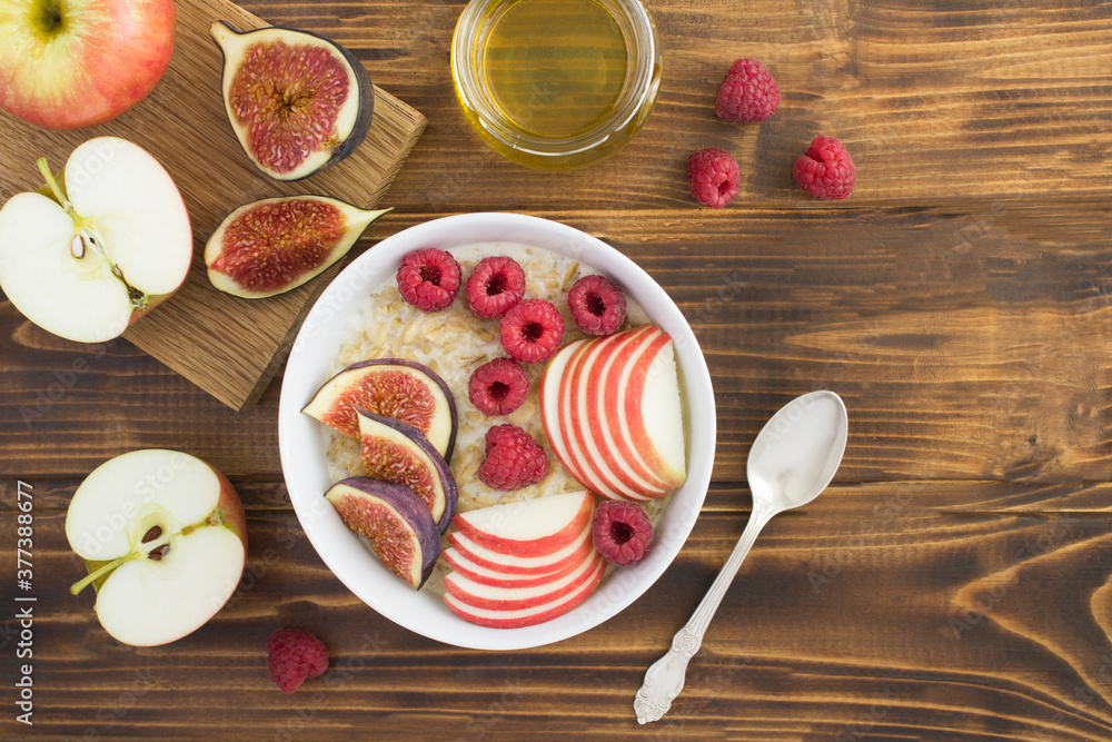 Top view of milk oatmeal with figs, raspberries and apple in the bowl on the wooden table Top view of milk oatmeal with figs, raspberries and apple in the bowl on the wooden table