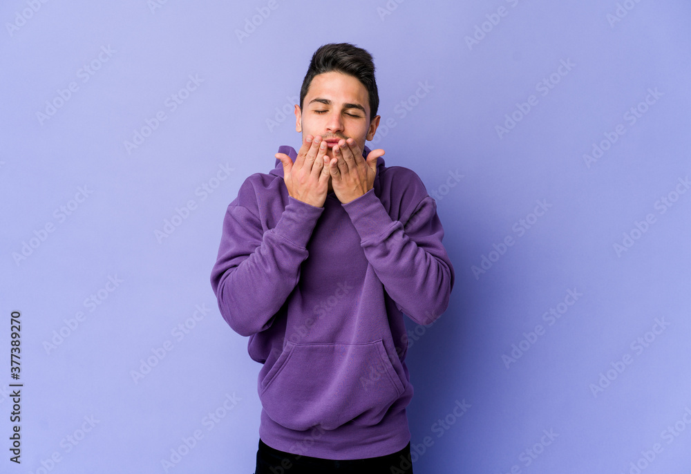 Young caucasian man isolated on purple background folding lips and holding palms to send air kiss. Young caucasian man isolated on purple background folding lips and holding palms to send air kiss.