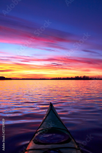 Bow of green kayak at colorful sunset over Danube river at autumn time