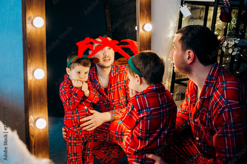 Happy family in red pajamas. Father with little son grimace in the mirror.