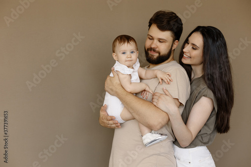 Portrait of young happy man and woman holding newborn cute babe dressed in white unisex clothing. Caucasian smiling father and mother embracing tenderly adorable new born child. Happy family concept