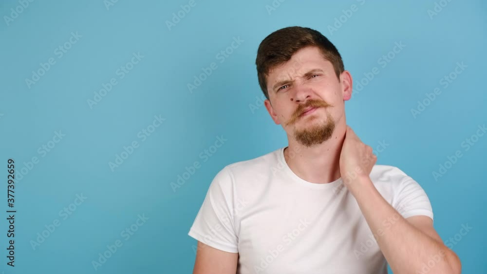 Unhappy young man isolated on blue studio background massaging hurt stiff neck, fatigued sad guy rubbing tensed muscles to relieve joint shoulder pain, dressed in white t-shirt. Fibromyalgia concept Unhappy young man isolated on blue studio background massaging hurt stiff neck, fatigued sad guy rubbing tensed muscles to relieve joint shoulder pain, dressed in white t-shirt. Fibromyalgia concept