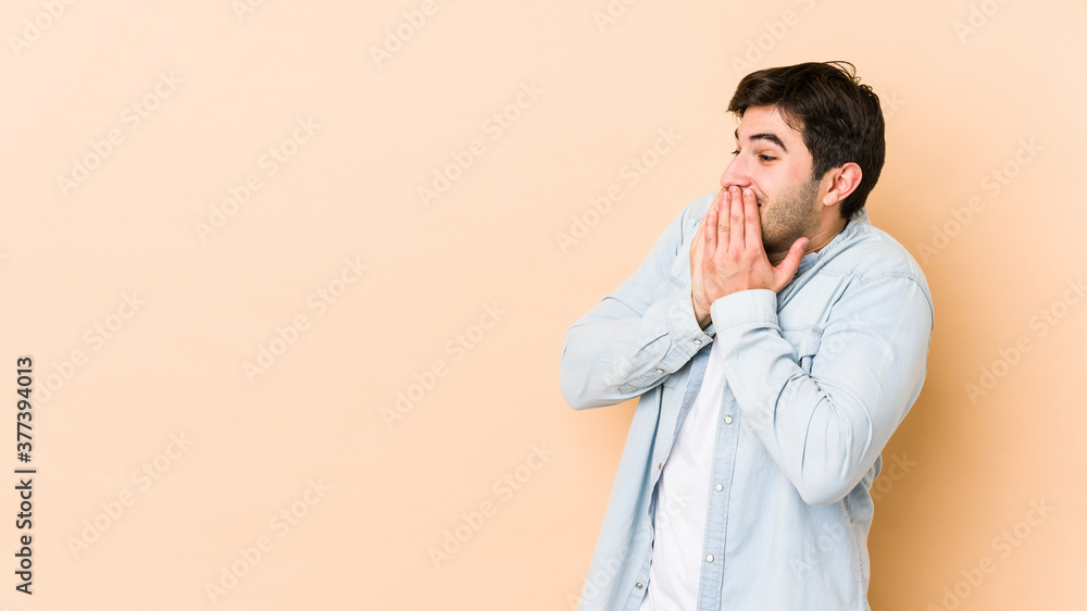 Young man isolated on beige background laughing about something, covering mouth with hands. Young man isolated on beige background laughing about something, covering mouth with hands.