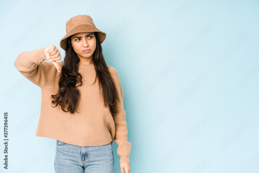 Young indian woman wearing a hat isolated on blue background showing thumb down and expressing dislike. Young indian woman wearing a hat isolated on blue background showing thumb down and expressing dislike.