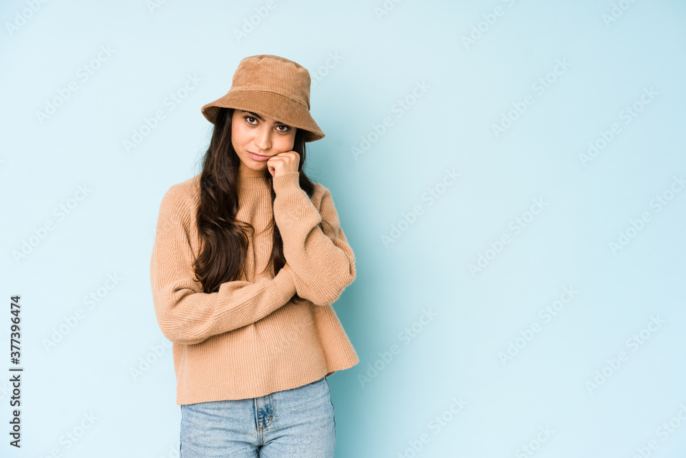 Young indian woman wearing a hat isolated on blue background who feels sad and pensive, looking at copy space. Young indian woman wearing a hat isolated on blue background who feels sad and pensive, looking at copy space.