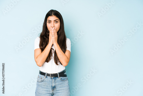 Young indian woman on blue background shocked, covering mouth with hands, anxious to discover something new.
