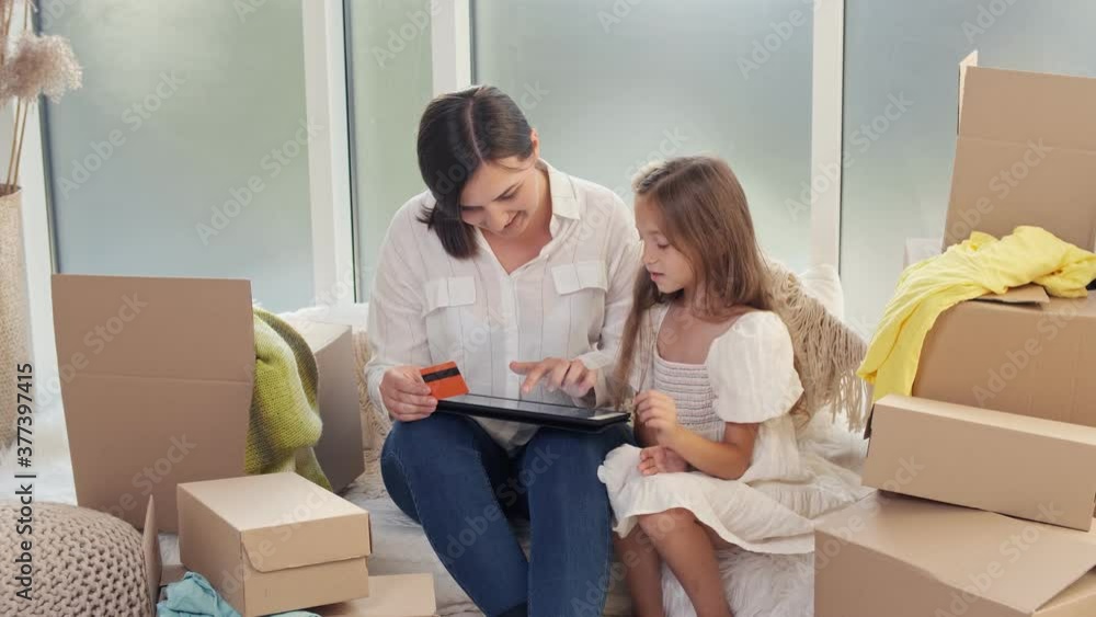Mother With Her Daughter Spending Money Together at Home. The Mother With a Child Uses a Credit Card for Online Shopping. Purchase Confirmation by the Internet. Uses a Tablet For Online Shopping. Mother With Her Daughter Spending Money Together at Home. The Mother With a Child Uses a Credit Card for Online Shopping. Purchase Confirmation by the Internet. Uses a Tablet For Online Shopping.