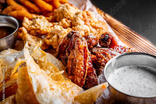 beer plate with spicy chicken wings, chips, fries onion rings, cheese balls, breaded, tartar sauce on wooden table