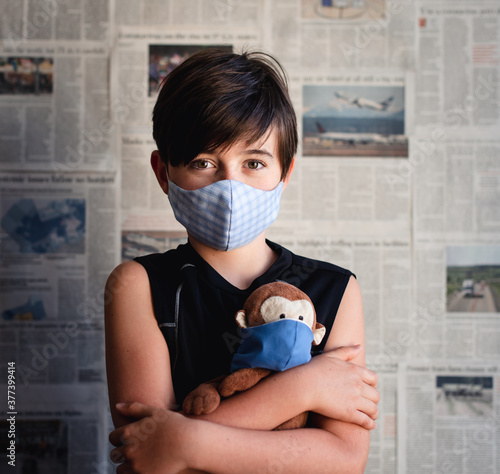 Portrait of boy wearing face mask holding toy monkey against newspaper clipping