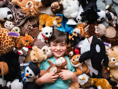 Happy young boy surrounded by his stuffed animals shot from above.