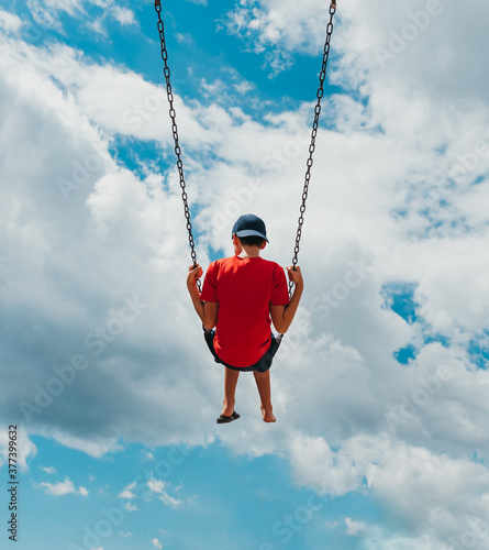 Rear view of boy on a swing with only cloudy sky in the background.