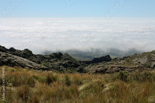 Sea of clouds. View of the hills, yellow grassland, sky and foamy clouds from the rocky mountaintop in a sunny day.  © Gonzalo