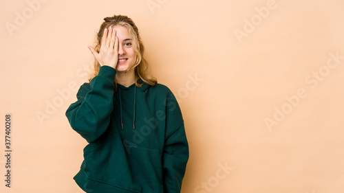 Young caucasian woman isolated on beige background having fun covering half of face with palm. © Asier