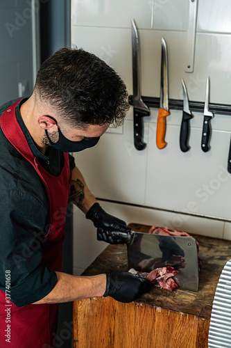 Butcher with mask cutting raw meat in the wood