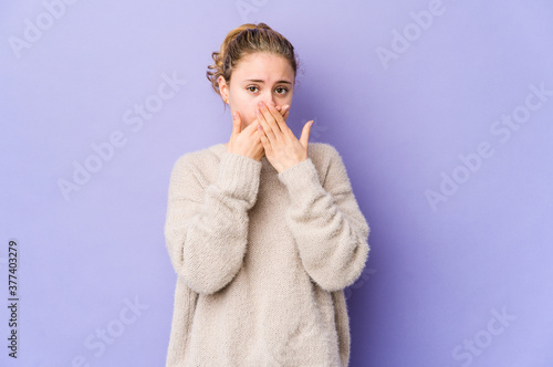 Young caucasian woman on purple background covering mouth with hands looking worried.