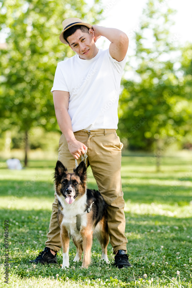 Obraz premium Young man walking his dog in the park. Latin model posing and watching on camera