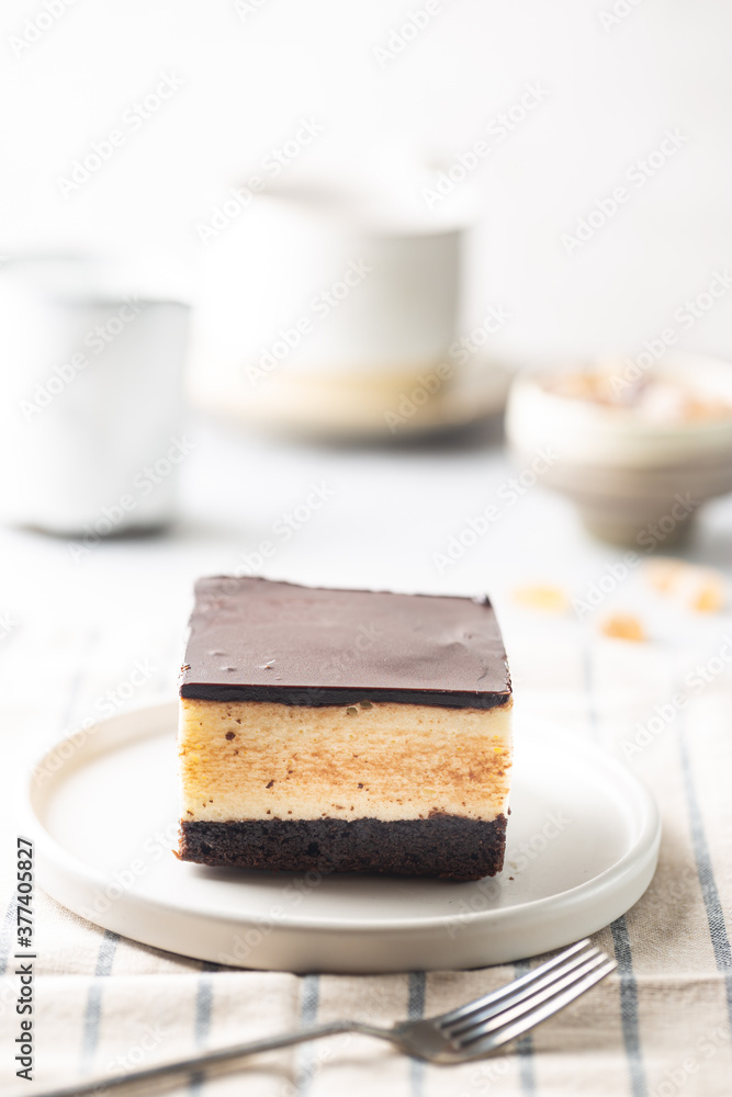 Piece of cake with souffle Birds milk, biscuit, mousse and dark chocolate on a white plate, light background Piece of cake with souffle Birds milk, biscuit, mousse and dark chocolate on a white plate, light background