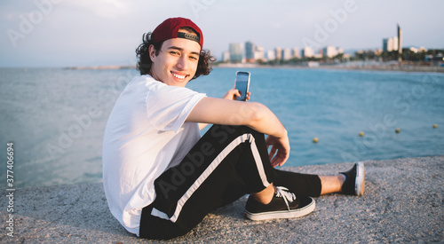 Smiling male sitting on seafront with mobile phone