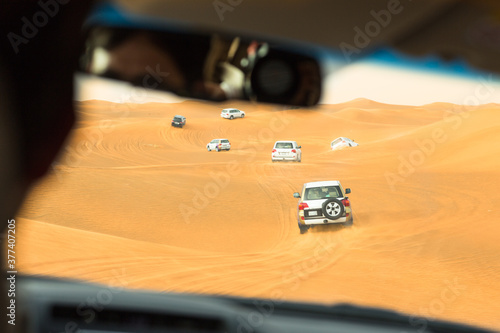 Fototapeta Naklejka Na Ścianę i Meble -  Group of 4x4 cars driving off-road in the desert sand dunes during a safari tour. Middle east tourist adventure.