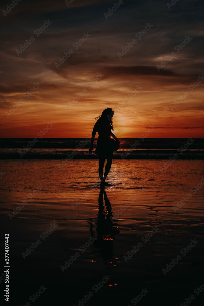 Paradise sunset woman silhouette against the orange evening sky. Perfect amazing travel destination in Indonesia, Bali, Kuta. Summer vacation concept.