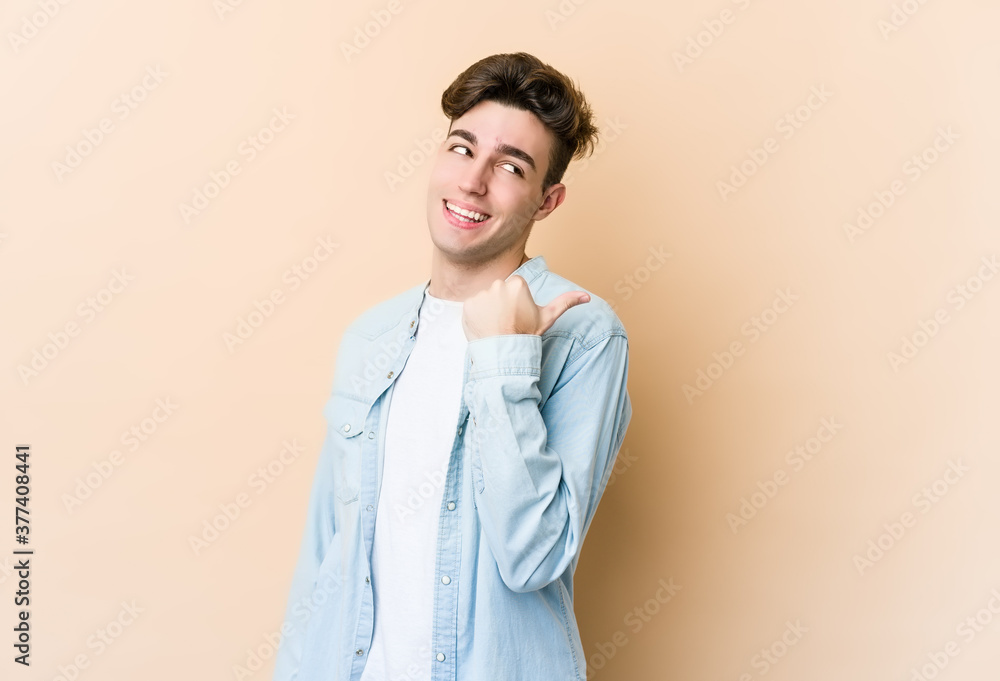 Young caucasian man isolated on beige background points with thumb finger away, laughing and carefree. Young caucasian man isolated on beige background points with thumb finger away, laughing and carefree.
