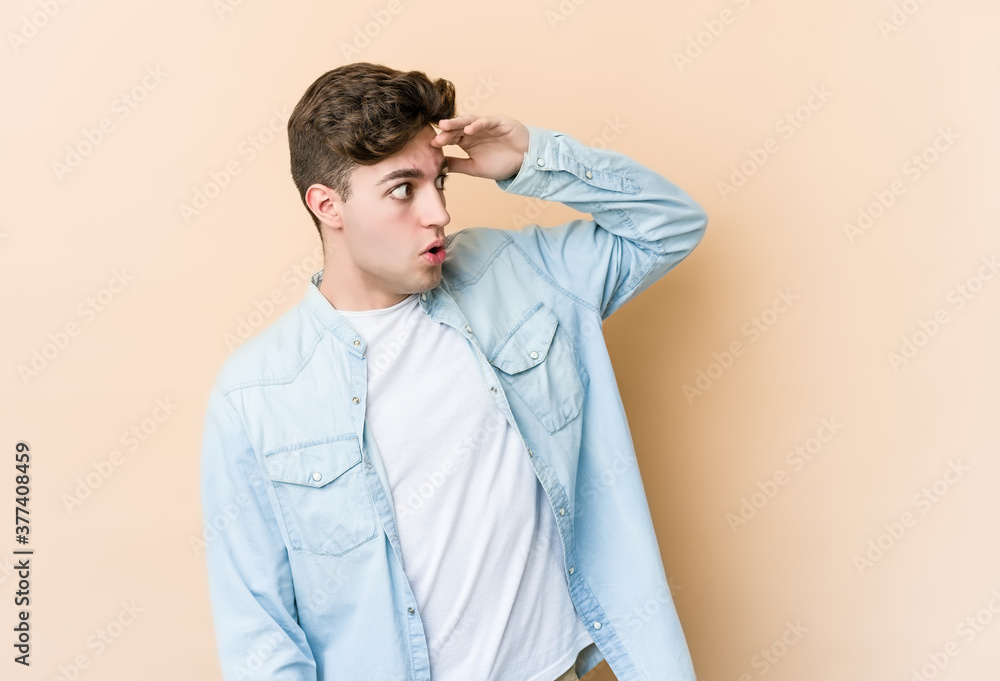 Young caucasian man isolated on beige background looking far away keeping hand on forehead. Young caucasian man isolated on beige background looking far away keeping hand on forehead.