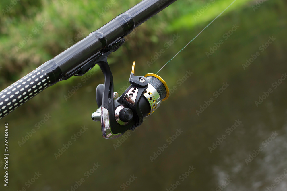 Fishing tackle. Reel on a fishing rod on the background of the river. Fishing tackle. Reel on a fishing rod on the background of the river.
