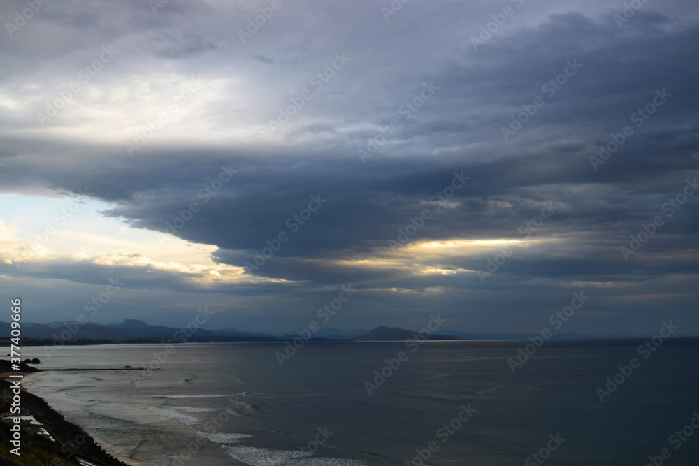 View of the coast and the sea with stormy clouds and mountains in the distance at sunset time
