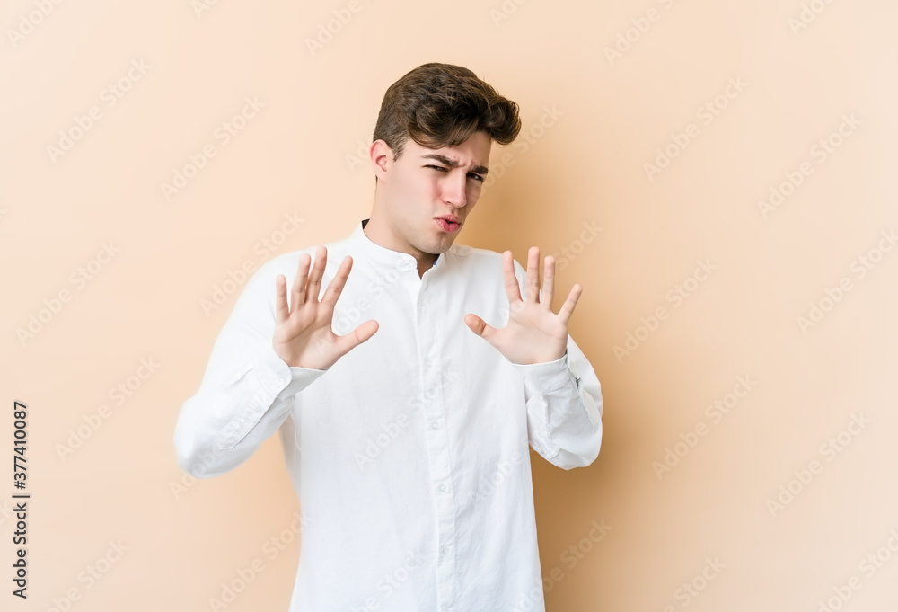 Young caucasian man isolated on beige background rejecting someone showing a gesture of disgust. Young caucasian man isolated on beige background rejecting someone showing a gesture of disgust.