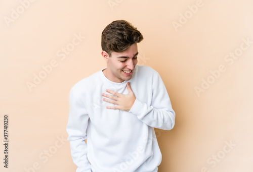 Young caucasian man isolated on beige background laughing keeping hands on heart, concept of happiness.