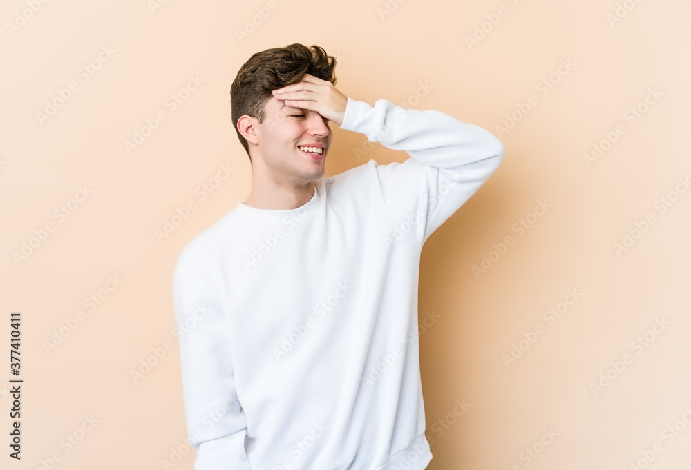 Young caucasian man isolated on beige background laughs joyfully keeping hands on head. Happiness concept. Young caucasian man isolated on beige background laughs joyfully keeping hands on head. Happiness concept.