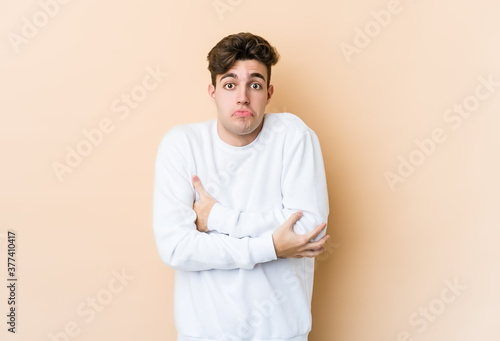 Young caucasian man isolated on beige background shrugs shoulders and open eyes confused.