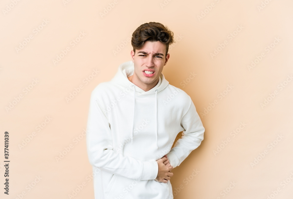 Young caucasian man isolated on beige background having a liver pain, stomach ache. Young caucasian man isolated on beige background having a liver pain, stomach ache.