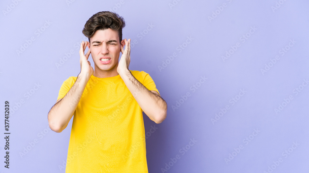 Young caucasian man isolated on purple background covering ears with fingers, stressed and desperate by a loudly ambient. Young caucasian man isolated on purple background covering ears with fingers, stressed and desperate by a loudly ambient.