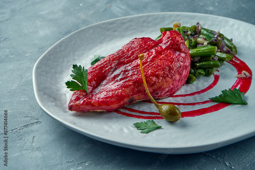 Baked chicken fillet in berry sauce with asparagus garnish with peanuts in a white plate on a gray background Baked chicken fillet in berry sauce with asparagus garnish with peanuts in a white plate on a gray background
