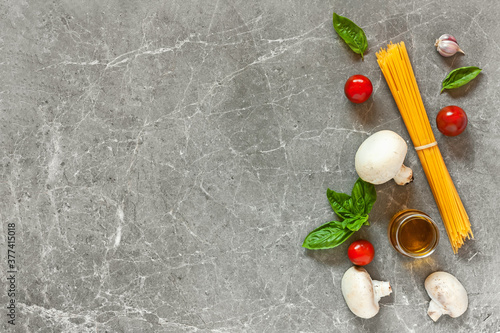 Top view of ingredients for pasta with mushrooms: spaghetti, basil, garlic,cherry and olive oil on gray stone background