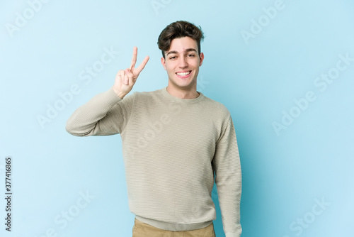 Young caucasian man isolated on blue background joyful and carefree showing a peace symbol with fingers.