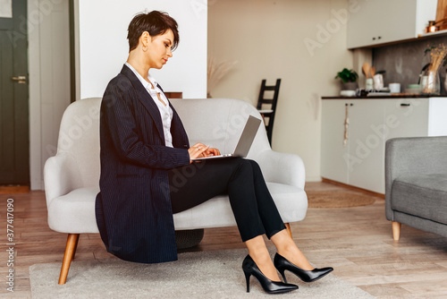 Young business woman working from home on laptop sitting on the sofa © Iryna