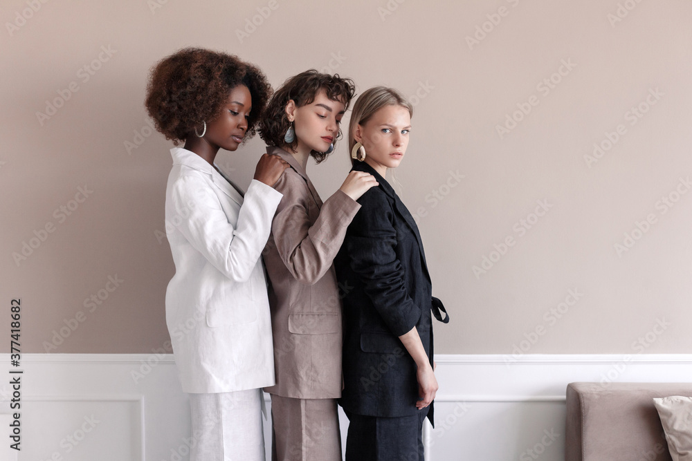 A small group of fashion multiracial multiethnic young beautiful sensual models are posing near the wall in studio room. Togetherness. A small group of fashion multiracial multiethnic young beautiful sensual models are posing near the wall in studio room. Togetherness.