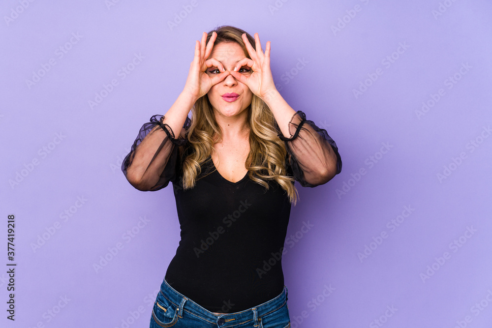 Young caucasian woman isolated on purple background showing okay sign over eyes Young caucasian woman isolated on purple background showing okay sign over eyes