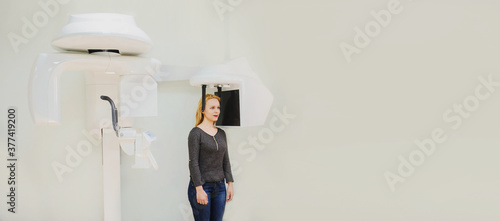 Close up portrait of young female dental patient standing in digital cephalometric panoramic x-ray machine. photo