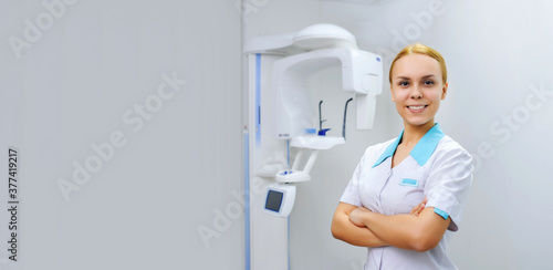 Portrait of a young woman dental x ray doctor smiling and looking at the camera in the background is panoramic teeth x ray orthopantomography machine.