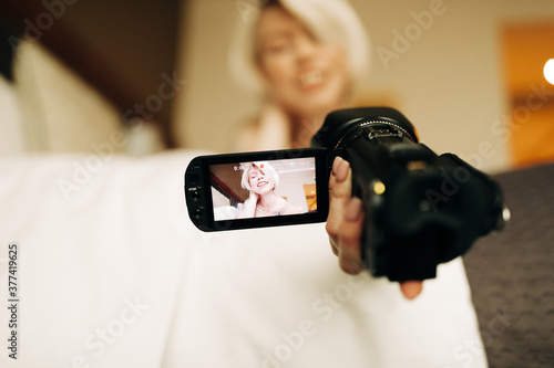 young blond woman with small camcorder on the bed