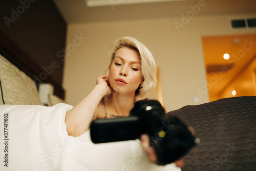 young blond woman with small camcorder on the bed photo