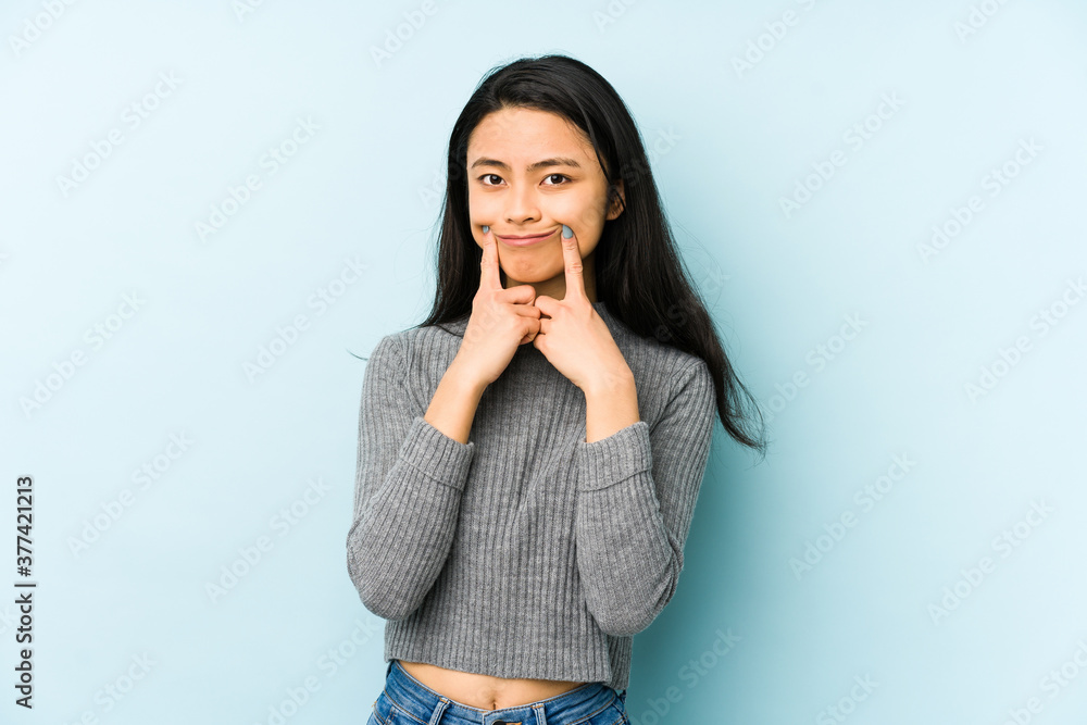 Young chinese woman isolated on a blue background doubting between two options. Young chinese woman isolated on a blue background doubting between two options.