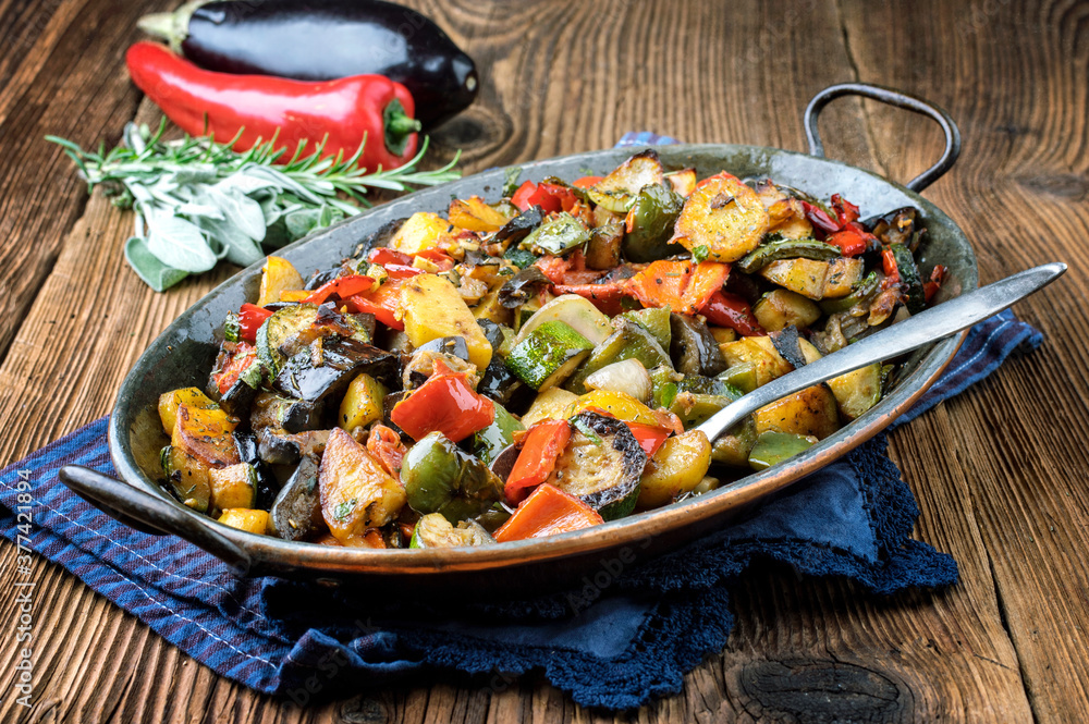 Traditional French vegetable ratatouile offered as close-up in a rustic casserole on a wooden table