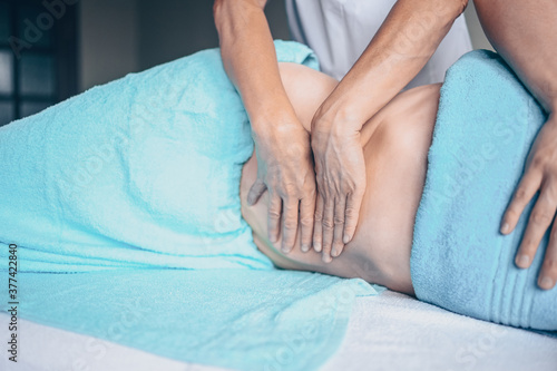 Young unrecognizable woman lying on massage table and enjoying therapeutic massage. Body care, losing weight concept. Hands masseur massage therapist doing anti-cellulite massage in spa clinic. © Алина Троева